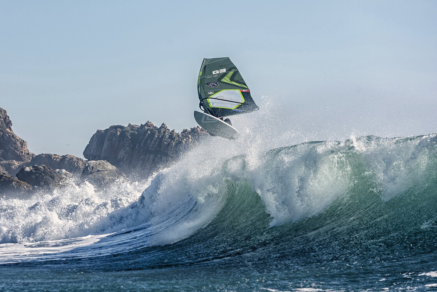 A windsurfer jumping a wave in front of the Matanzas rocks